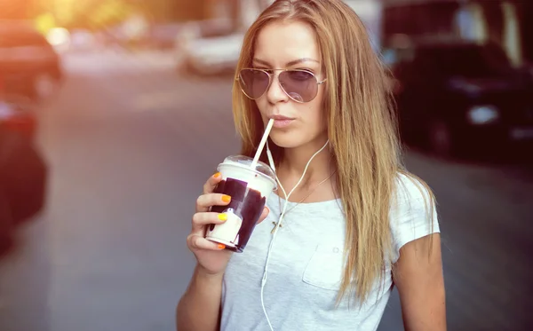 Söt flicka med mjölk shake lyssnar musik på gatan. Sunset. — Stockfoto