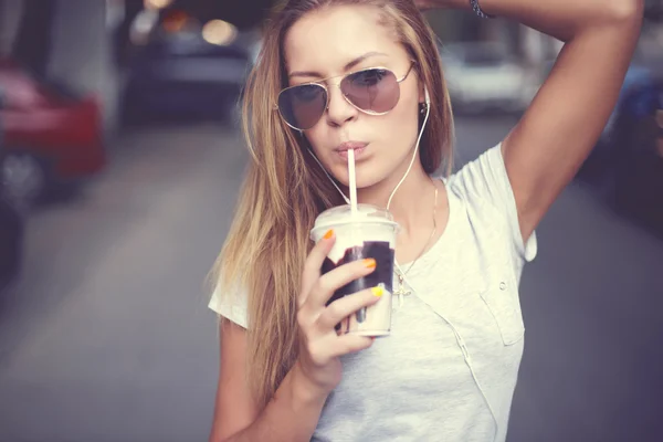 Mooi meisje met milkshake luisteren muziek op de straat. Zonsondergang. — Stockfoto