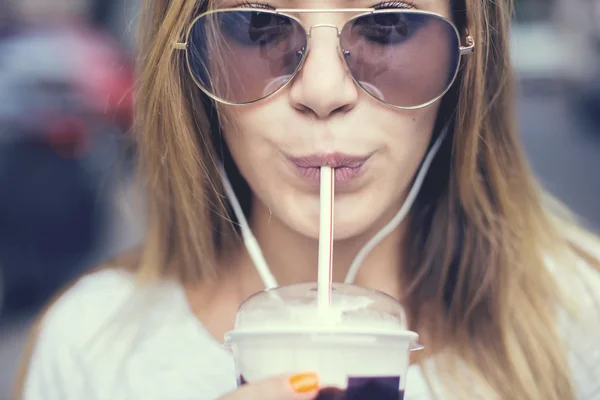 Mooi meisje met milkshake luisteren muziek op de straat. Zonsondergang. — Stockfoto