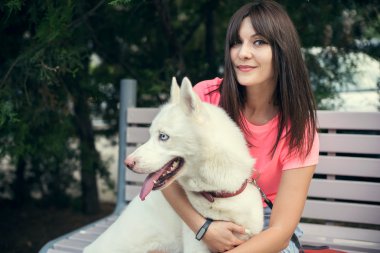 Bankta oturan ve beyaz husky köpeğiyle oynayan genç kız