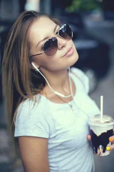 Mooi meisje met milkshake luisteren muziek op de straat. Zonsondergang. — Stockfoto