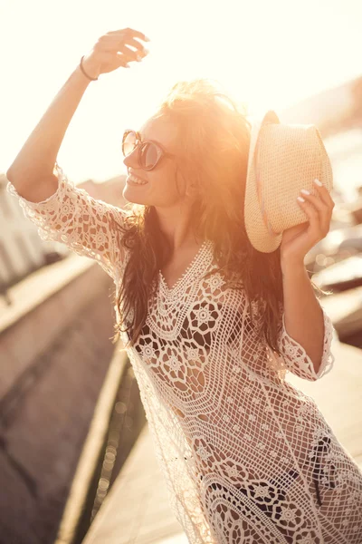 Młoda kobieta w kapeluszu i słodkie lato sukienka stojąc na molo w spokojnej miejscowości scenerii, patrząc na zachód słońca — Zdjęcie stockowe