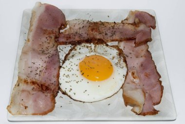 Beyaz arka planda kare tabakta servis edilen pastırmalı sahanda yumurta.