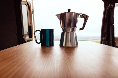 Aqua bialetti kahve makinesi ve kamp kupası bir T4 karavanın ahşap masasında.