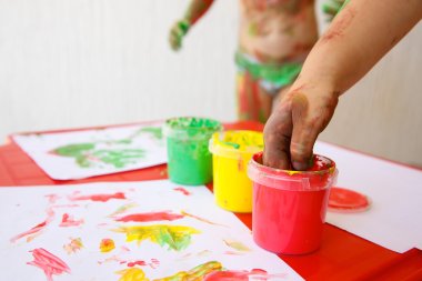 Child dipping fingers in non-toxic finger paints clipart