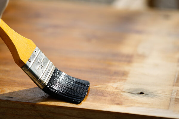 Paintbrush sliding over wooden surface, protecting wood 