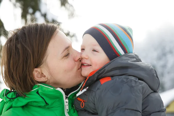 Madre besando a su hijo en un paisaje nevado de invierno — Foto de Stock