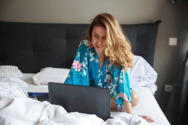 Gecelik giymiş seksi bir kadın, yatakta oturuyor, bilgisayardan erkek arkadaşıyla görüntülü görüşme yapıyor. Uzak mesafe ilişkisi, sosyal uzaklık kavramı.