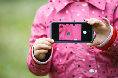 Little girl holding a smart phone with picture on display clipart