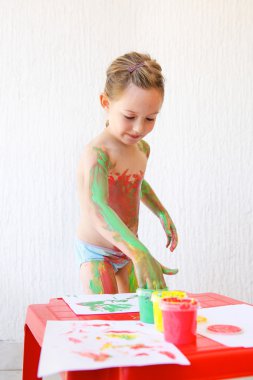 Little girl body painting herself with finger paints clipart