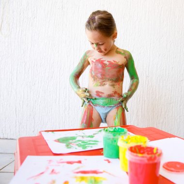Little girl body painting herself with finger paints clipart