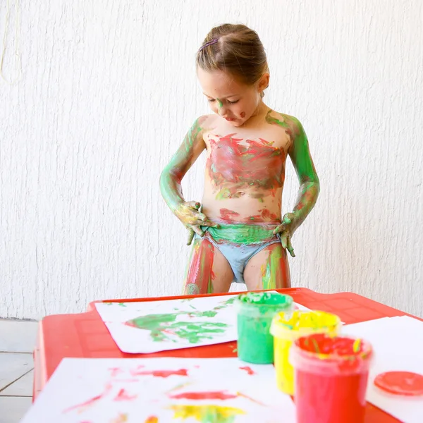 Little girl body painting herself with finger paints — Stockfoto