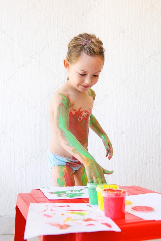 Little girl body painting herself with finger paints