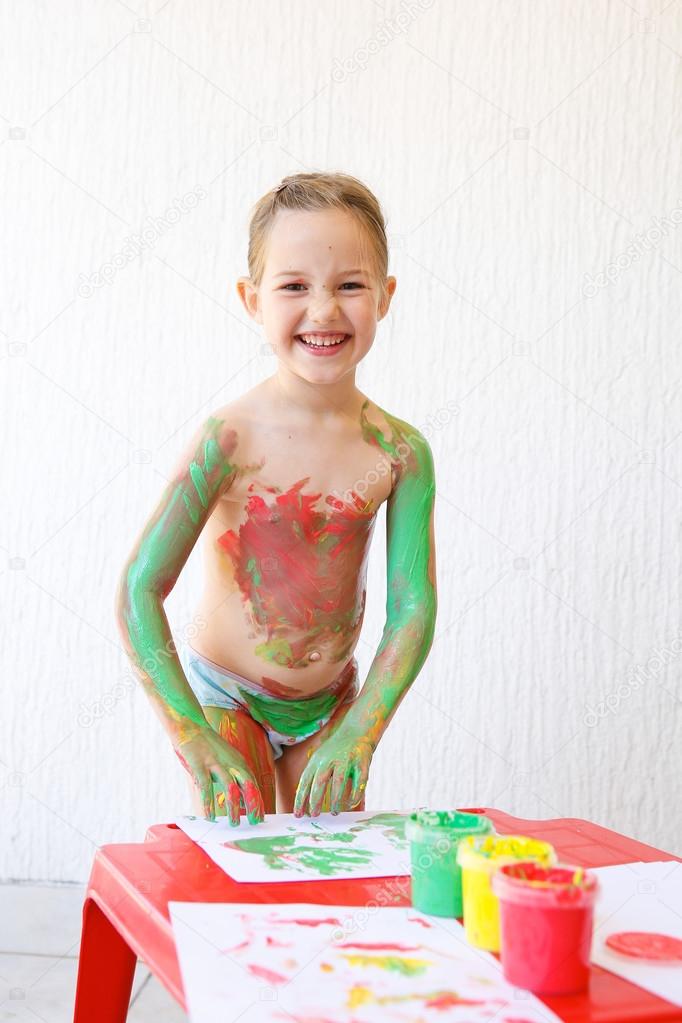 Little girl body painting herself with finger paints