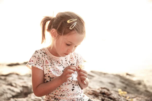 Little girl sitting on a sunlit beach at sunset, playing — Stock Photo, Image