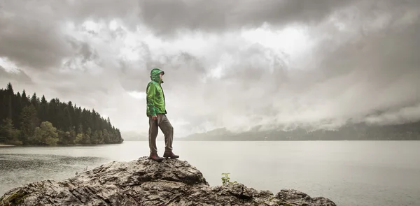 Człowiek stojący na skale obok jeziora górskiego w deszczu — Zdjęcie stockowe