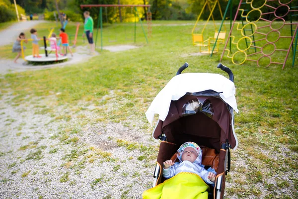 Bambino che riposa in un passeggino sul parco giochi — Foto Stock