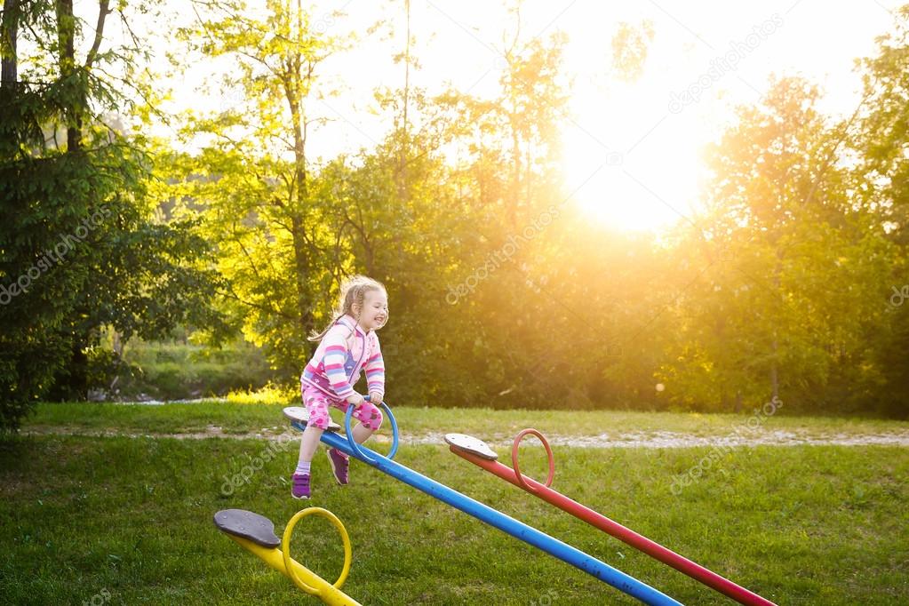 Happy little girl playing, going up ad down on a seesaw