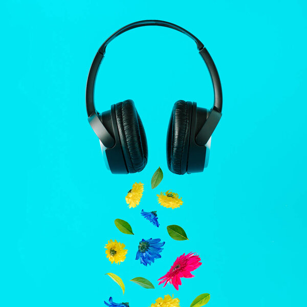 Advertisement idea with black music headphones, colorful summer flowers and green leaves against pastel blue background. Minimal nature concept.