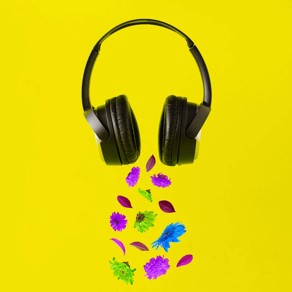 Advertisement idea with black music headphones, colorful summer flowers and green leaves against pastel yellow background. Minimal nature concept.
