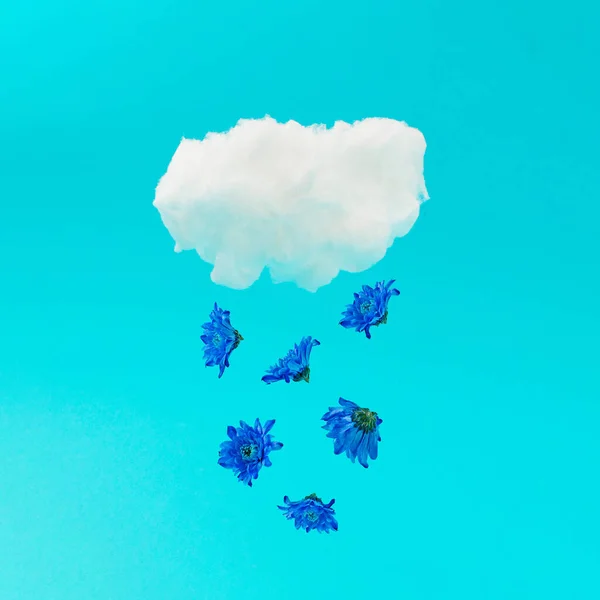A rain of blue flowers falls from the cloud against pastel blue background. Minimal summer nature ad concept idea.