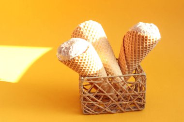 Dondurma ve waffle külahı güneşte duruyor, sarı arka planda, yan görünüşte.