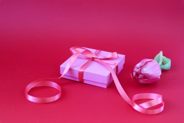 Kırmızı pruvalı bir hediye kutusu, kırmızı bir zemin üzerinde kırmızı lale, metin için boşluk