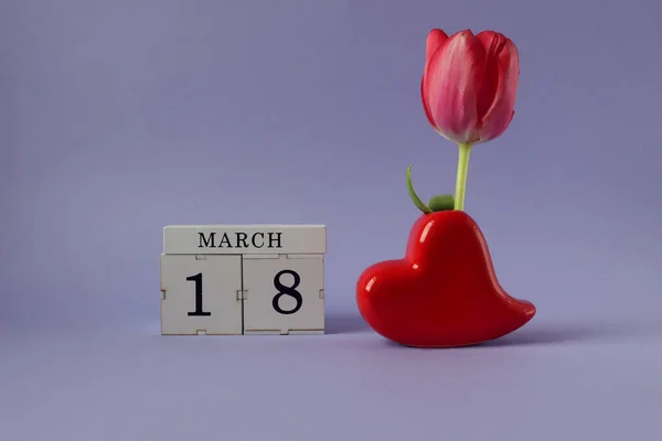 Calendar for March 18: cubes with the number 18, the name of the month March in English, a heart-shaped vase with a scarlet tulip on a pastel background