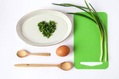 Beyaz tabakta dilimlenmiş yeşil soğan, yeşil kesme tahtası, yeşil soğan, yumurta ve tahta kaşıklar beyaz arka planda - vitamin sağlıklı yiyecek kavramı