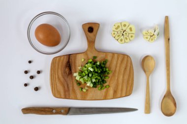 Mutfak aletleri ve yumurtalar arasında ahşap bir kesme tahtasındaki yeşil soğanlar.