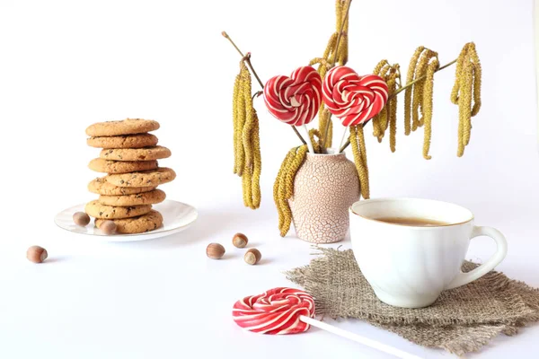 Oatmeal cookies with a cup of tea, a bouquet of flowering hazel branches, lollipops in the form of hearts - the concept of a pleasant tea party on spring days