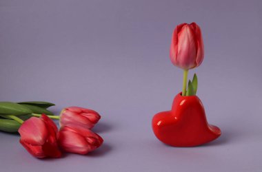 Kırmızı lale, kalp şeklinde vazo. Pastel arka planda kırmızı lale var.