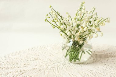 Şeffaf cam vazoda vadideki zambaklar dantel peçeteye yakın dursun.