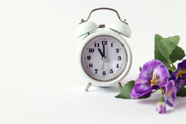 White alarm clock with viola flower on white background, side view, space for text