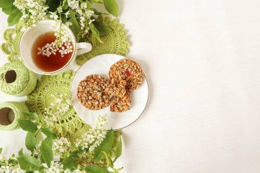 Kiraz dallı bir fincan çay, iplik ve el yapımı motifler, beyaz arka planda kurabiyeler, üst manzara, metin için boşluk