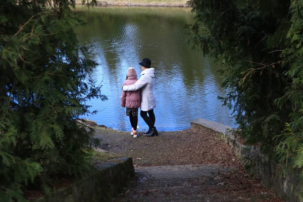 Two female silhouettes on the lake shore in the old park on a spring day, side view