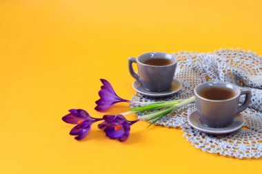 İki gri kahve fincanı, gri bir peçetede kır çiçekleri, sarı arka plan, yazı için boşluk.