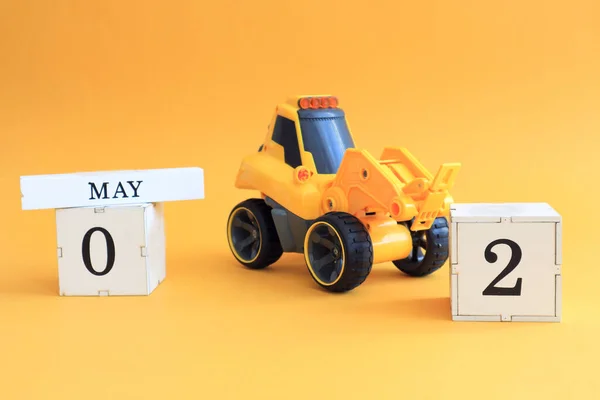Calendar for May 2: a toy yellow tractor with numbers on cubes 0 and 2, the name of the month in English on a yellow background