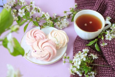 Tabakta pembe marşmelovlar, örülmüş leylak ürününde bir fincan çay, kiraz çiçekleri, bokeh