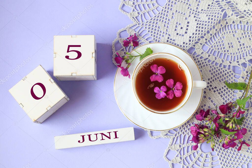 Calendar for June 5: cubes with the numbers 0 and 5, the name of the month of June in English, a cup of tea with purple flowers in it, a gray openwork napkin on a light background, top view