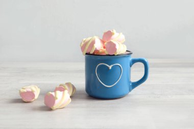İyi bir sabah ve keyifli bir ruh hali. Üzerinde kalp resmi olan mavi bir bardak, gri arka planda pembe hava şekerlemeleriyle dolu, yakın plan, metin için alan