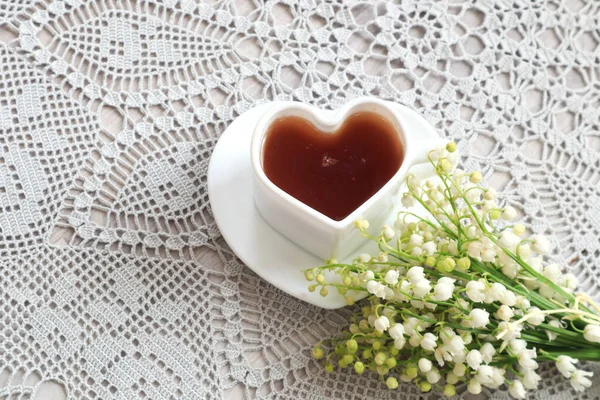 The concept of good morning and good mood. A bouquet of lilies of the valley , a cup of tea in the shape of a heart on a gray napkin, top view, close-up
