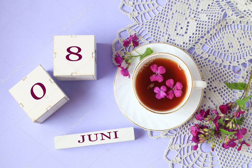 Calendar for June 8: cubes with the numbers 0 and 8, the name of the month of June in English, a cup of tea with purple flowers in it, a gray openwork napkin on a light background, top view