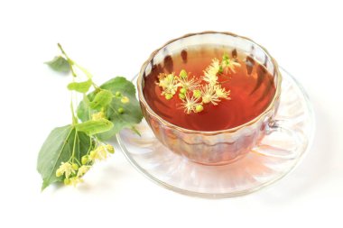 Şifalı bitkisel çay içme kavramı. İçinde ıhlamur çiçekleri olan bir fincan çay, arka planda yeşil dallar, yakın plan..