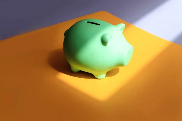 The concept of accumulation of financial resources. Piggy bank in the shape of a pig on different backgrounds-yellow and lilac, in the sun and with shadows from objects, side view, space for text