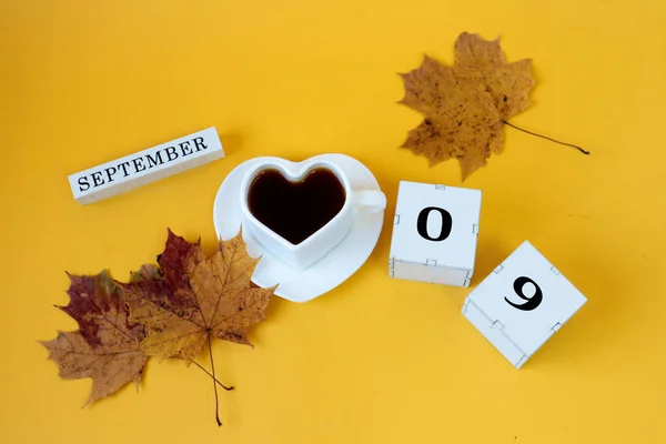 九月九日的日历 一个月的英文名 方块的数字为0和9 茶碟上有一个白色的心形杯子 黄色背景 顶视图 — 图库照片