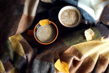 Sıcak bir sonbahar konsepti. Sıcak kahve fincanı, ekose atkı, sarı huş yaprağı, üst manzara, yazı yazılacak bir yer.