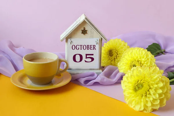Calendar for October 5 : decorative house with the name of the month in English with the numbers 05, a bouquet of yellow dahlias on a light pastel scarf, side view, multi-colored background
