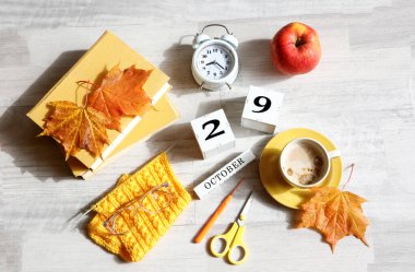 29 Ekim takvimi: İngilizce ayın adı, 29 numaralı küpler, kitaplar, çalar saat, akçaağaç yaprakları, kırmızı elma, bir fincan kahve, gri arka planda gözlük.