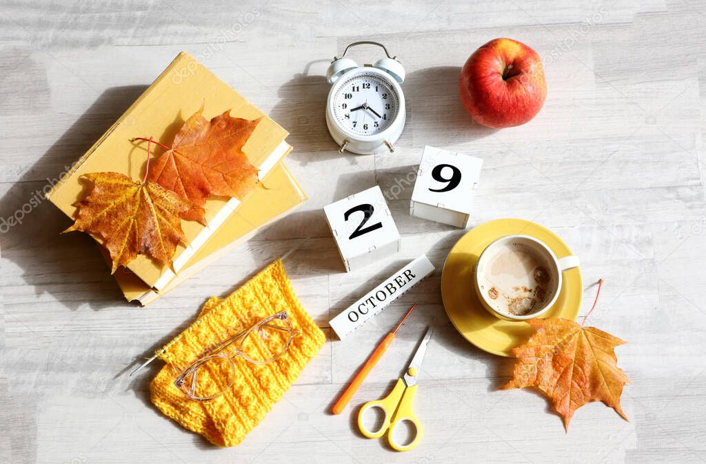 Calendar for October 29 : the name of the month in English, cubes with the number 29, books, an alarm clock, maple leaves, a red apple, a cup of coffee, eyeglasses on a gray background